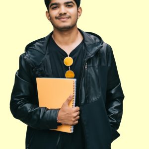 Confident college student in a black jacket holding a yellow notebook against a light background.